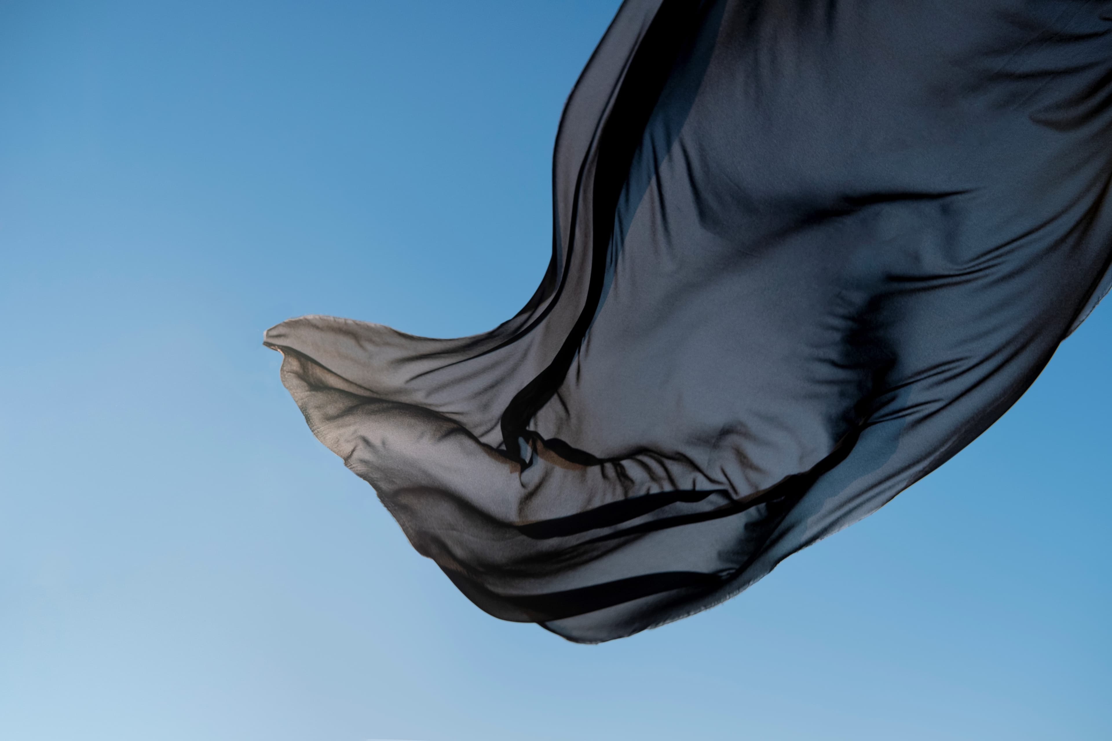 A black niqab caught mid-motion against open sky, backlit by low sun.