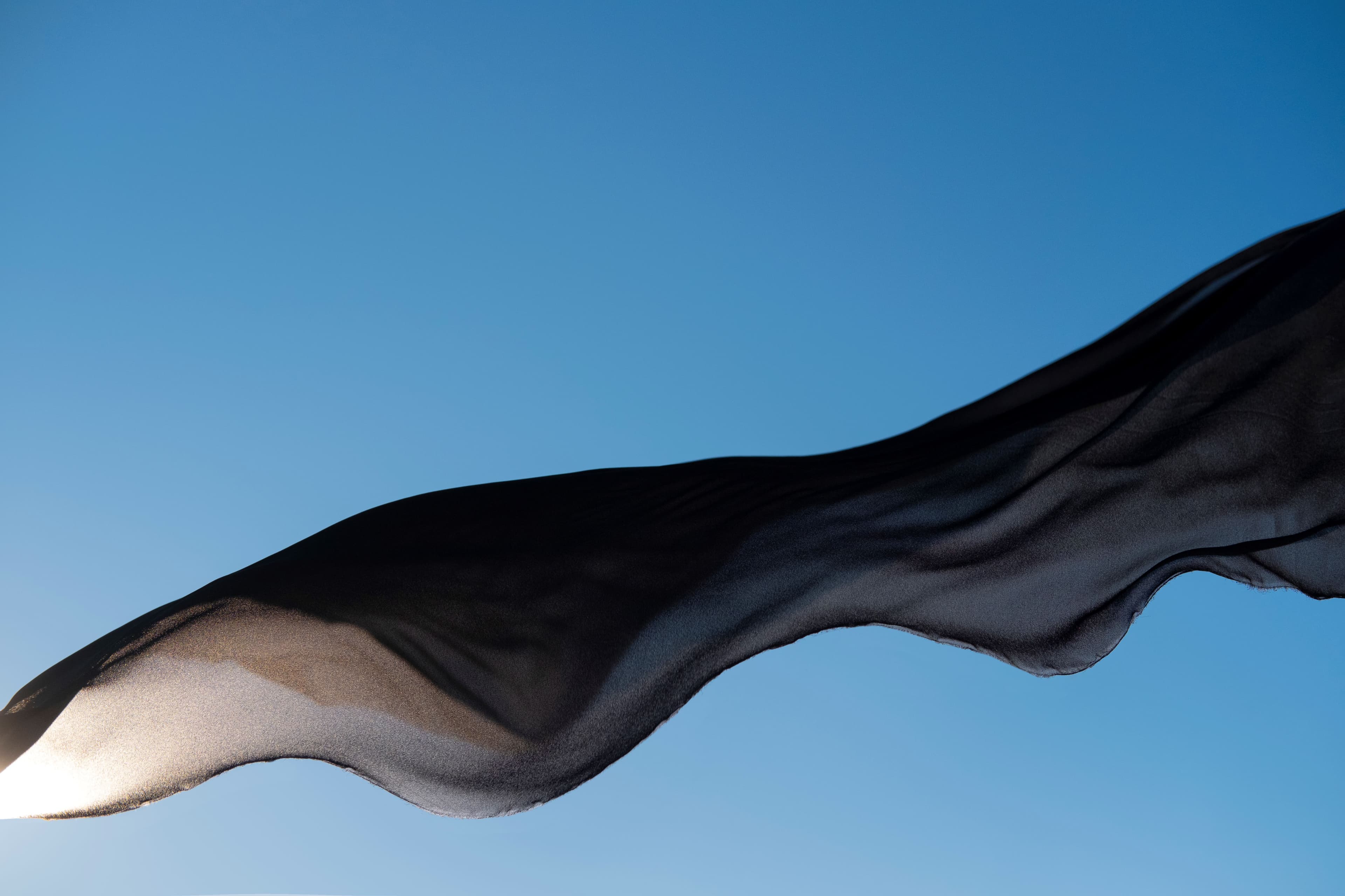 A dark niqab streaming sideways in the wind against a clear blue sky, rim-lit by the sun.