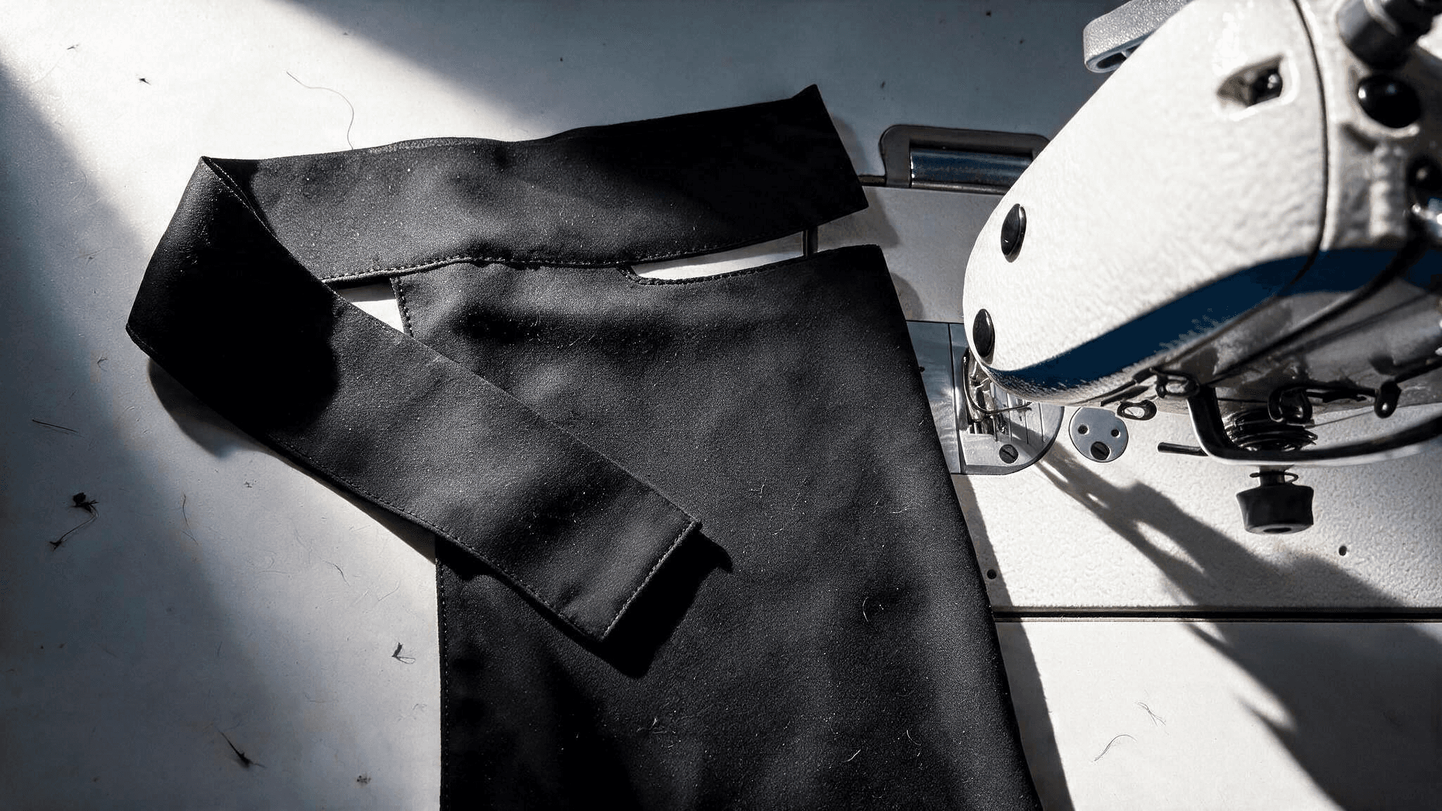A half-finished black niqab under the presser foot of a sewing machine, its seams and the slit for the eyes still being stitched.